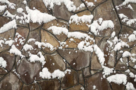 Wall from multi-coloured stones of the various form fastened by clay under snowの写真素材