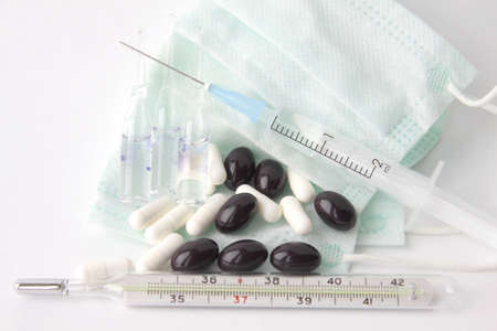 Scattered tablets lay on a gauze bandage between a syringe and a thermometer