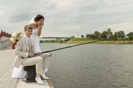 Joyful newly-married couple fishes on a pierの写真素材