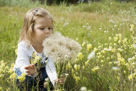 girl sits among a grass on a glade and plays with a dandelionの写真素材