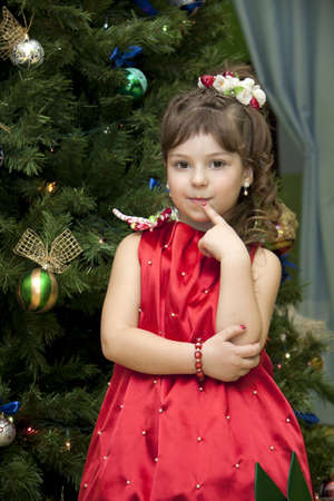 little girl in the strawberry dress costs near the decorated fur-tree and waits for a giftの写真素材