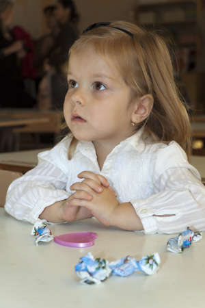 small child sits at a school desk in a class and attentively listens  Candy wrappers and a pocket mirror nearby lieの写真素材