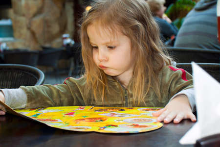 little girl sits at a table and looks in the menu  To make the orderの写真素材