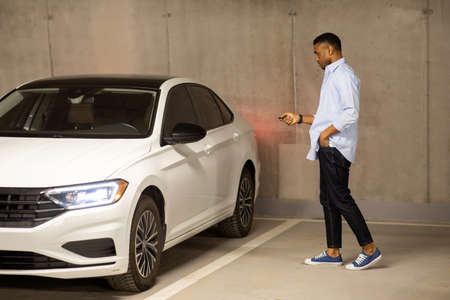 African american man opens his car with keys in an underground parking lot while talking on the...