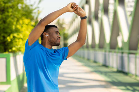 Portrait of an african american sportsman warming up his arms before training using a music app on...