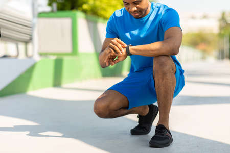 African-American urban jogger on a big bridge checking his smartwatch before starting his run