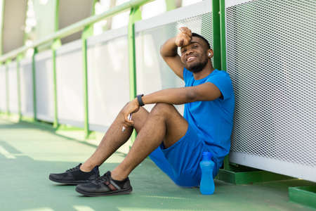 Happy african american sportsman sitting on sports track feeling tired