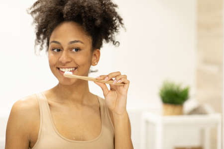 Happy girl looks in the mirror using an ecological toothbrush with whitening toothpaste.