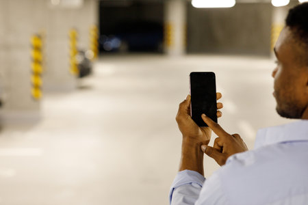 Hand of man hold mobile phone over blurred car parking with bokeh light Backgroundの写真素材