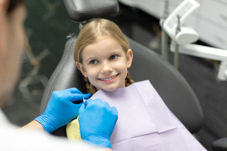 Cute child girl preparation for examination and treatment of oral cavity, dentist puts napkin on girl looking at doc and smilingの写真素材