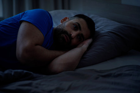 Depressed man in pajamas lies in his bed and feels badの写真素材