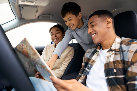 Road trip adventure. Happy family of three with boy looking at map sitting in car and choosing destination. Travel by automobileの写真素材