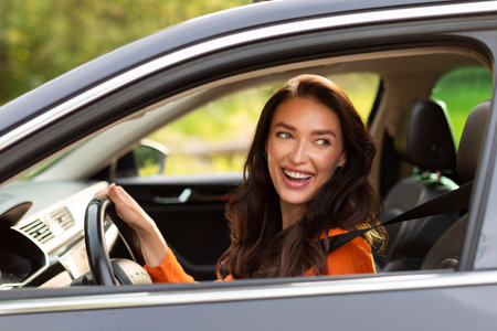 Enjoying trip. Happy young European woman sitting in new car, holding steering wheel and smiling,...