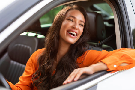 Portrait of young beautiful woman sitting in luxury car looking out of window and smiling, enjoying automobile after test driveの写真素材