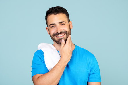 Photo of young happy man enjoying fresh perfectly smooth skin touching beard isolated on blue backgroundの写真素材