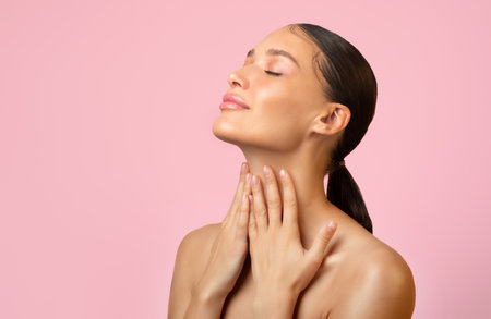 Attractive adorable serene young woman touching pure neck skin isolated over pink background, free spaceの写真素材