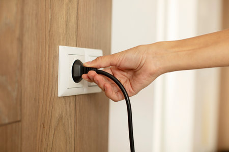 Woman putting on or removing electric plug cable in socket, closeup. Electrical equipment wires and...