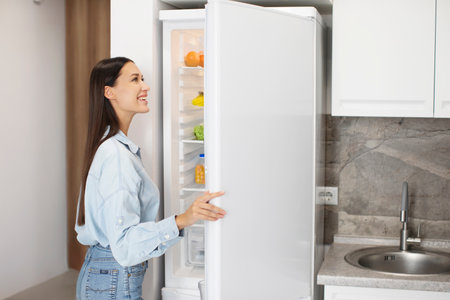 Lady looking inside of fridge while standing in kitchen, opening refrigerator and searching for food, rear view with copy spaceの写真素材