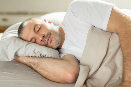 Asleep European middle aged man resting peacefully in comfortable bed, lying with closed eyes under blanket. Time to rest and nap conceptの写真素材
