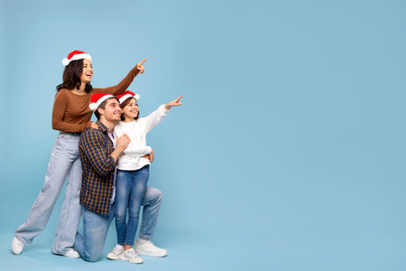 Wow Christmas offer. Excited European family of three in Santa hats pointing finger aside, showing free space for Xmas ad over pink backgroundの写真素材
