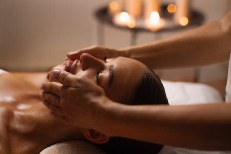 Face building concept. Young woman receiving total relaxation, having face massage at serene atmosphere in spa salon with candles on background.の写真素材