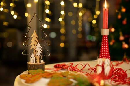 Merry Christmas. Candle, decorations, plate with gingerbread cookies on table and glowing garlands on backgroundの写真素材