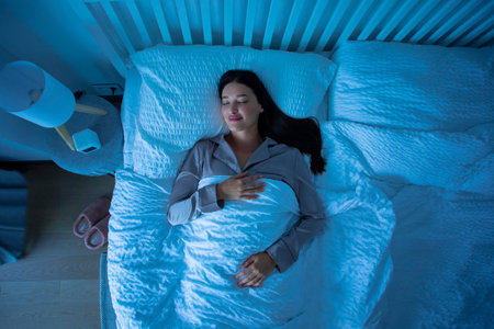 Serene relaxed woman sleeping on soft pillow, wearing pajamas resting under warm blanket in...