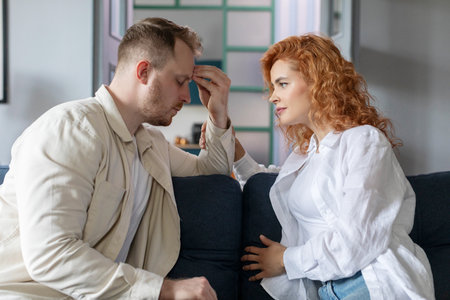 Caring wife calming sad husband, sitting face to face on sofa in living room. Relationship problems,...