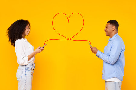 Black lady and guy chatting online, typing love sms on smartphone, messaging via phones connected with drawn heart shape stringの写真素材