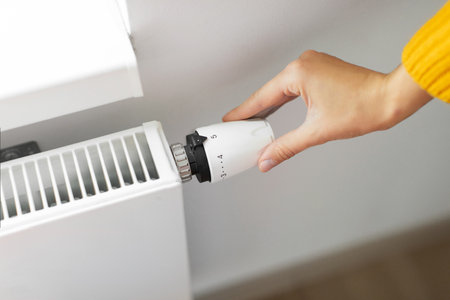 Hand of young woman changing the temperature on the radiator by temperature controller, turn the heating on to maximumの写真素材