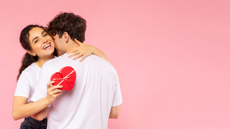 Happy European couple hugging, lady holding heart shaped gift box and embracing her man, celebrating Valentines Day on pink background, free space, bannerの写真素材