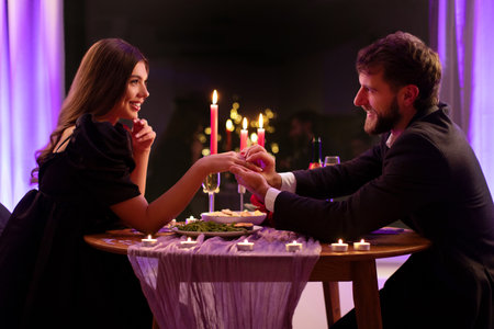 She said yes. Man wearing marriage ring to his beloved ladys finger, getting engaged in restaurant during romantic dateの写真素材