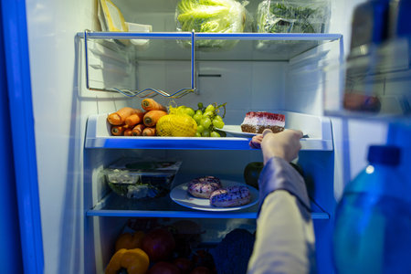 POV view of young lady taking plate with cake from fridge, eating late at night. Food conceptの写真素材