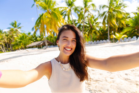 Happy smiling young woman taking selfie on beach, enjoying vacation on tropical island, palms on backgroundの写真素材