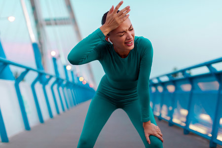 Tired woman catching her breath during training outdoors, stopping while running on bridgeの写真素材