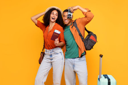 Joyful Latin tourists couple posing with passport and tickets and man holding retro camera, standing on yellow background, ready for vacationの写真素材