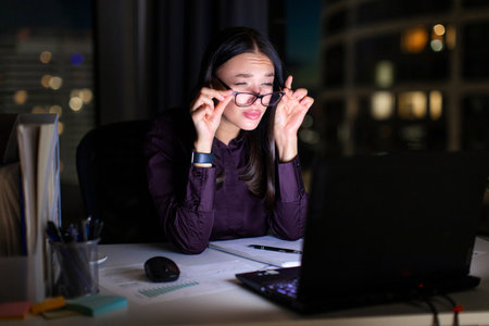Overworked tired business person taking off glasses and squinting her eyes, working on laptop late at night, feeling lack of sleep, having eyestrain problemの写真素材