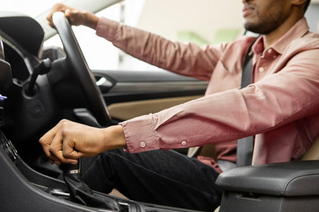 Closeup shot of black man holding steering wheel and gear shift looking at road, sitting in modern...