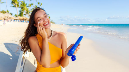 Beautiful woman applying sun block cream on face and smiling, sitting on sun lounger on the beach...