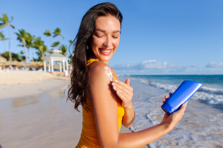 Beautiful lady applying sun cream on tanned shoulder, using sun protection, holding suntan lotion...
