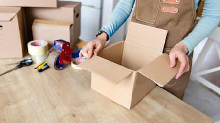 Small business owner preparing parcel for dispatch, folding cardboard box and packing online orders. Workflow of online store merchant using sales platformの写真素材