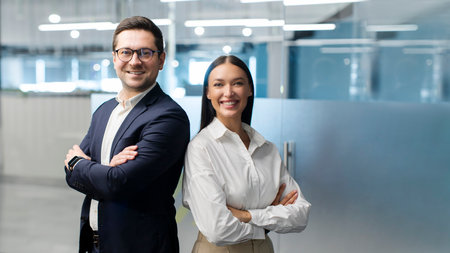 Two European business colleagues standing with arms crossed and smiling at camera, posing in modern...