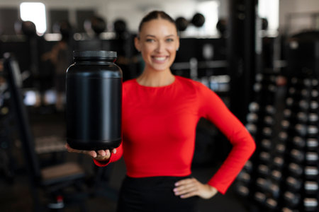 Sports nutrition ad. Fit woman with protein whey powder in black container standing in gym interior...