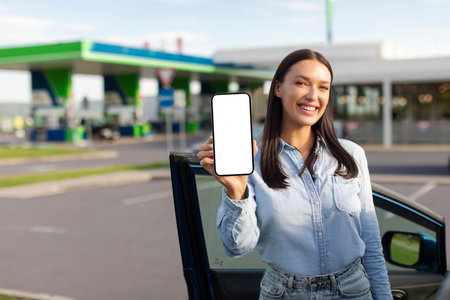 Happy young lady showing cellphone with blank screen for mockup of ECO fuel online shopping app,...