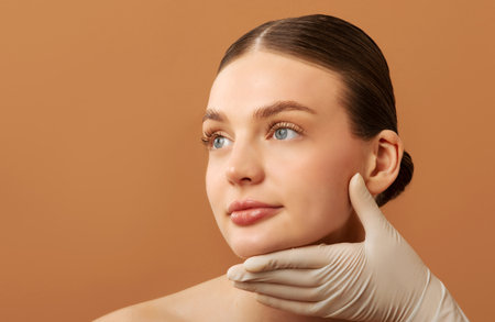 Cosmetic surgery concept. Doctor examining ladys face over beige studio background, woman during...