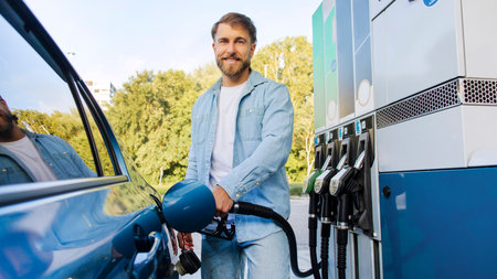 Man refilling auto with bio fuel at modern petrol station, male driver smiling at camera, panorama shot. Automobile fueling offerの写真素材