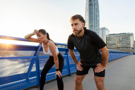 Tired young couple runners taking breath after hard workout outdoors, resting, standing on city...