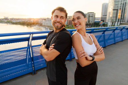 Smiling young man and woman in sportswear enjoying workout break, standing back to back and smiling outdoorsの写真素材