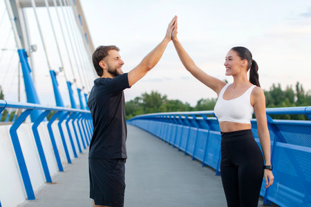 Happy sporty man and woman giving high five each other, rejoicing success in sport training after workout outdoors. Healthy lifestyle conceptの写真素材