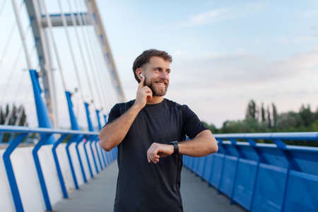 Happy young man in earphones enjoy outdoors workout, male jogger listening music and checking health data on smartwatch during trainingの写真素材